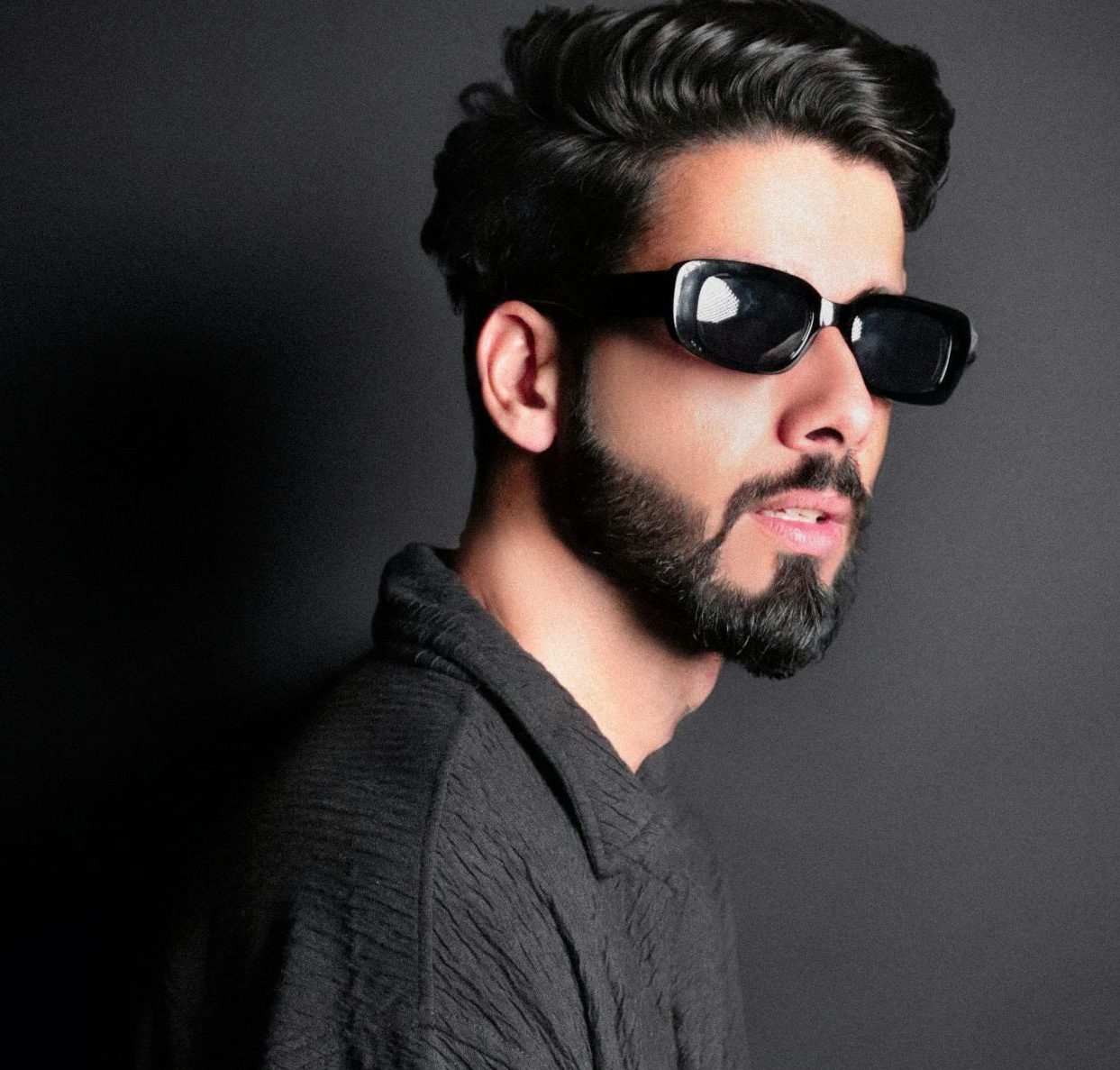 Fashionable portrait of a stylish man wearing sunglasses against a dark background.