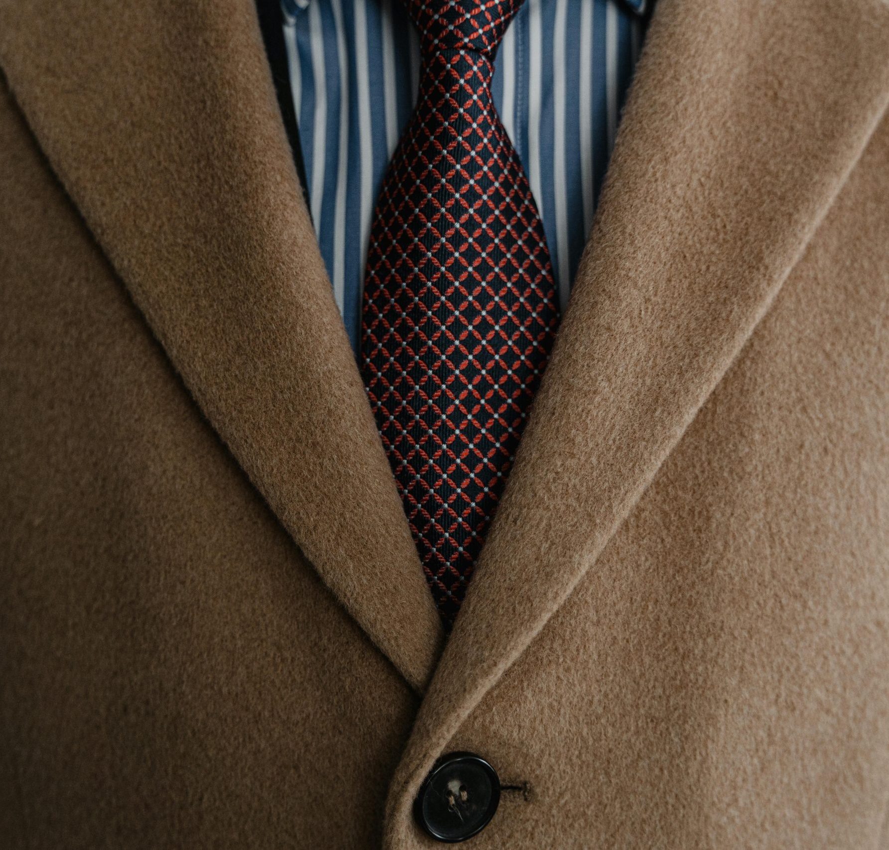 Close-up of a sophisticated brown wool coat over a striped shirt and patterned tie.