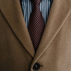 Close-up of a sophisticated brown wool coat over a striped shirt and patterned tie.